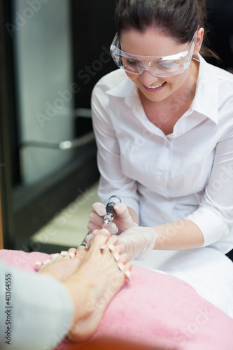 Photo: Nail technician removing callus at feet Nail technician removing callus at feet