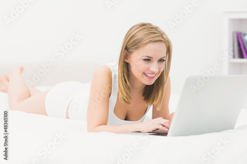 Photo: Beautiful happy woman lying in bed and using laptop Beautiful happy woman lying in bed and using laptop