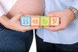 Mother and father to be holding wooden blocks that spell baby