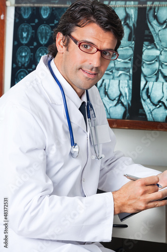 Photo: Male Doctor Sitting At Desk Male Doctor Sitting At Desk