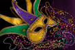 A Mardi gras jester's mask with beads on a black background