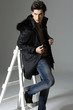 Shot of a young man in coat sitting wooden ladder