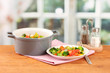 Vegetable stew in gray pot on wooden table on bright background