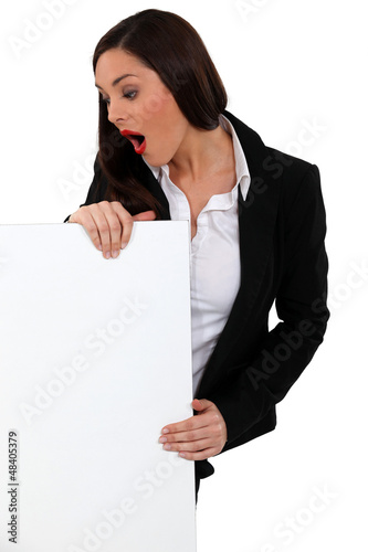 Photo: Shocked businesswoman stood with blank poster Shocked businesswoman stood with blank poster