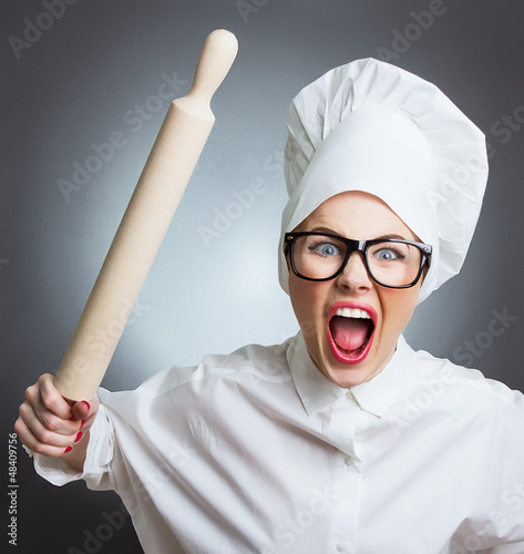 Photo: Angry woman cook trying to hit with a rolling pin over a gray Angry woman cook trying to hit with a rolling pin over a gray