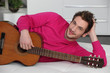 Man laying on sofa with acoustic guitar