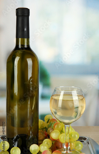 Photo: White wine in glass with bottle on salver on room background White wine in glass with bottle on salver on room background
