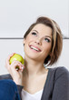 Sitting on the sofa woman eats a green apple