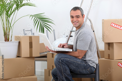 Photo: Man using a laptop computer sitting amongst cardboard boxes Man using a laptop computer sitting amongst cardboard boxes