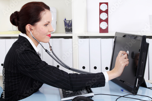 Photo: Businesswoman with sthetoscope checking pc Businesswoman with sthetoscope checking pc