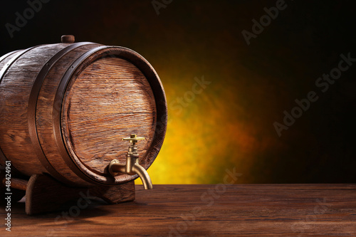 Photo: Old oak barrel on a wooden table. Behind blurred dark background Old oak barrel on a wooden table. Behind blurred dark background