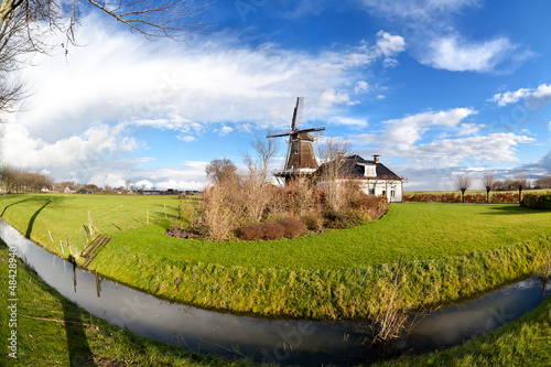 Photo: Dutch windmill by canal on green pasture Dutch windmill by canal on green pasture