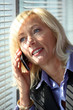 Blond woman making phone call by window blinds