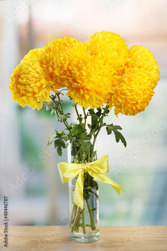 Photo: bright yellow chrysanthemums in glass vase, on wooden table bright yellow chrysanthemums in glass vase, on wooden table