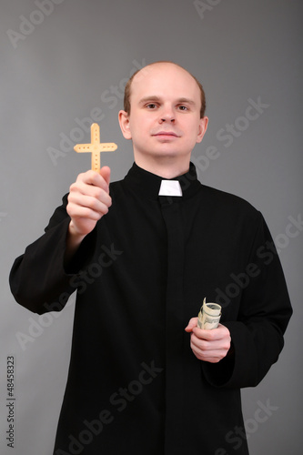 Photo: Young pastor with cross and money on gray background Young pastor with cross and money on gray background