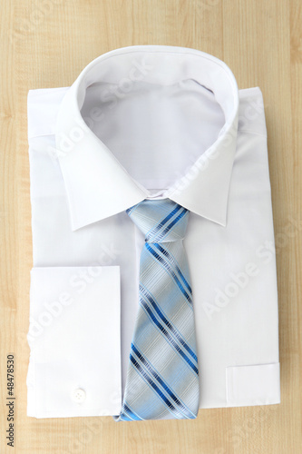 Photo: New white man's shirt with color tie on wooden background New white man's shirt with color tie on wooden background