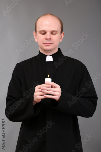 Photo: Portrait of young Pastor holding candle in his hand,on gray Portrait of young Pastor holding candle in his hand,on gray