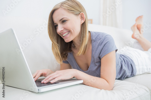 Photo: Casual woman lying on couch and using laptop Casual woman lying on couch and using laptop