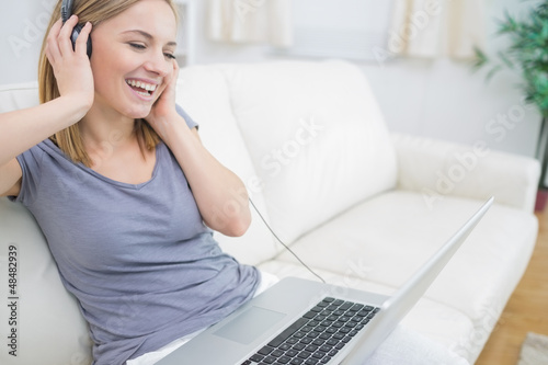 Photo: Happy woman listening music through headphones with laptop Happy woman listening music through headphones with laptop