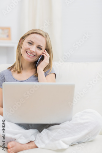 Photo: Portrait of casual woman using laptop and cellphone at home Portrait of casual woman using laptop and cellphone at home