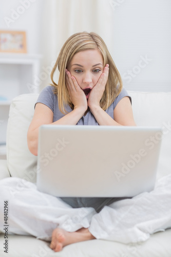 Photo: Shocked casual woman looking at laptop screen at home Shocked casual woman looking at laptop screen at home