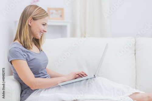 Photo: Side view of casual woman using laptop on sofa Side view of casual woman using laptop on sofa