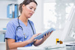 Female surgeon using digital tablet in front of computer at clin