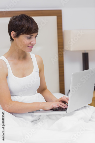 Photo: Smiling woman using laptop in bed Smiling woman using laptop in bed