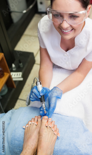 Photo: Nail technician removing callus at feet Nail technician removing callus at feet