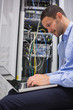 Photo: Man using laptop beside servers Man using laptop beside servers