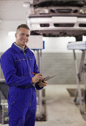 Photo: Smiling mechanic writing on a clipboard Smiling mechanic writing on a clipboard