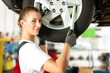 Female car mechanic working on jacked auto