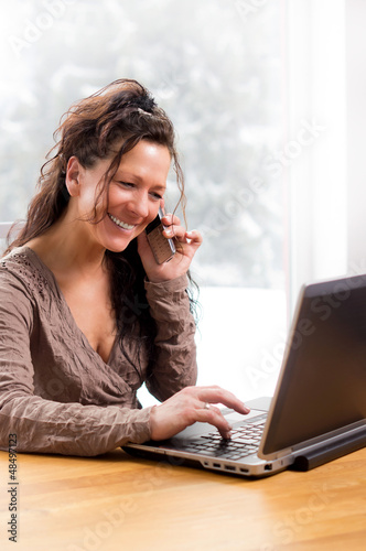 Photo: Lachende Frau telefonierend vor Notebook Lachende Frau telefonierend vor Notebook
