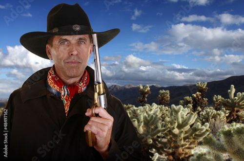 Photo: Cowboy with gun touching hat in cholla garden Cowboy with gun touching hat in cholla garden
