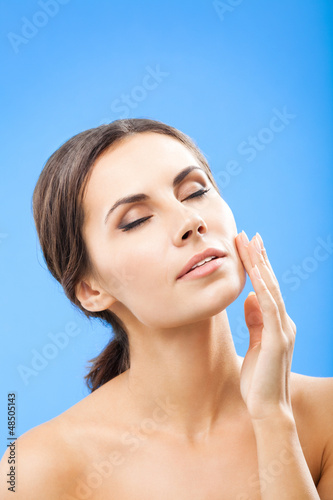 Photo: Woman touching skin or applying cream, over blue Woman touching skin or applying cream, over blue