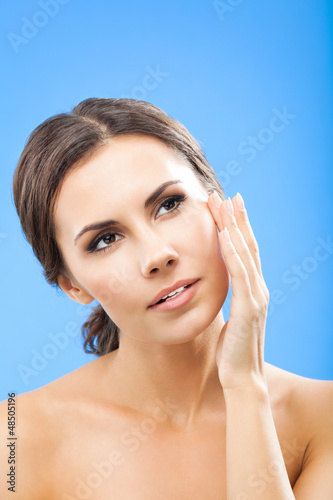 Photo: Woman touching skin or applying cream, over blue Woman touching skin or applying cream, over blue