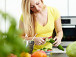 Young woman making salad in kitchen, cutting a cucumber