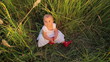 Cute baby in a white dress sitting in tall grass