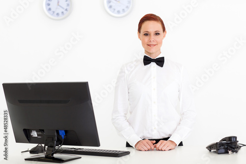 Photo: pretty young receptionist standing by hotel reception pretty young receptionist standing by hotel reception
