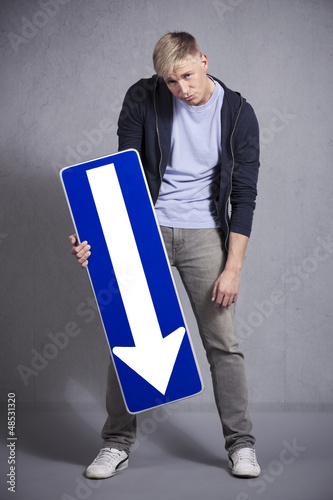 Photo: Miserable man holding direction arrow sign pointing down. Miserable man holding direction arrow sign pointing down.