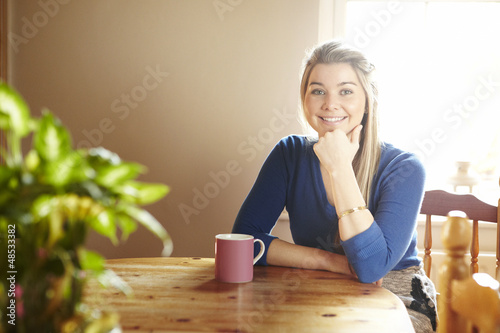 Photo: Young woman sitting at table smiling Young woman sitting at table smiling