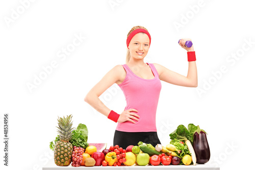 Photo: Young woman holding a dumbbell and posing with a pile of food Young woman holding a dumbbell and posing with a pile of food