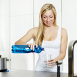 Woman infusing a drinking glass with water in a kitchen