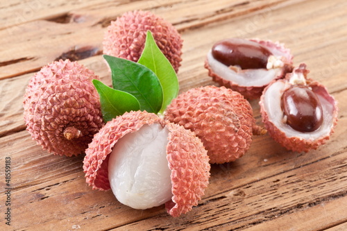 Photo: Lychee with leaves on a wooden table. Lychee with leaves on a wooden table.