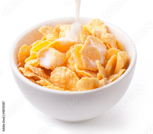 Photo: Milk pouring into a bowl of corn flake isolated on white Milk pouring into a bowl of corn flake isolated on white