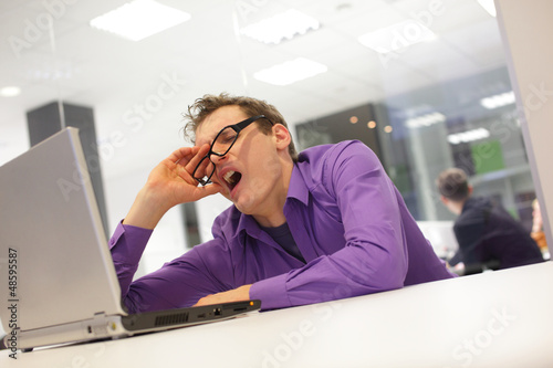 Photo: bored yawning businessman with laptop in the office bored yawning businessman with laptop in the office
