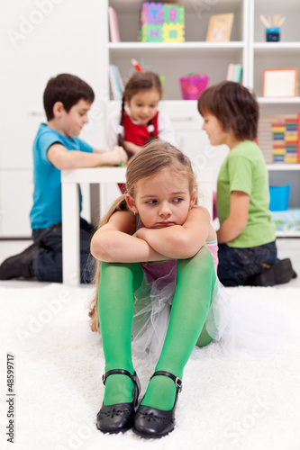Photo: Sad little girl sitting excluded by the other kids Sad little girl sitting excluded by the other kids