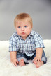 Little boy sitting on white carpet on gray background