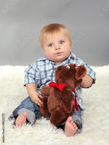Photo: Little boy sitting on white carpet on gray background Little boy sitting on white carpet on gray background
