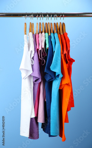 Photo: Variety of casual shirts on wooden hangers,on blue background Variety of casual shirts on wooden hangers,on blue background